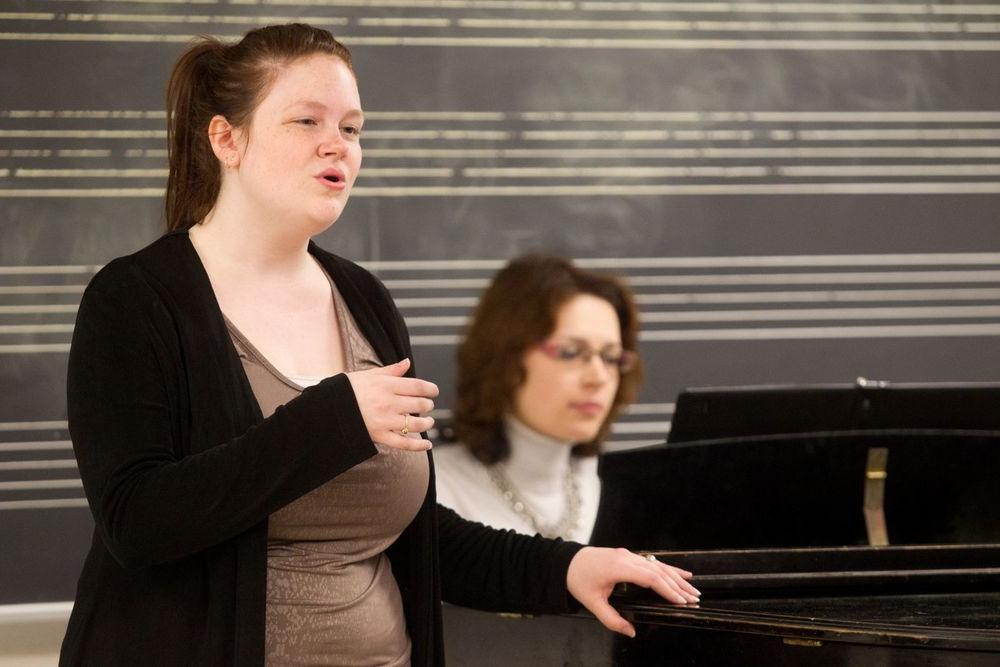 博耶音乐舞蹈学院的一名学生在唱歌，一名女子在弹钢琴.